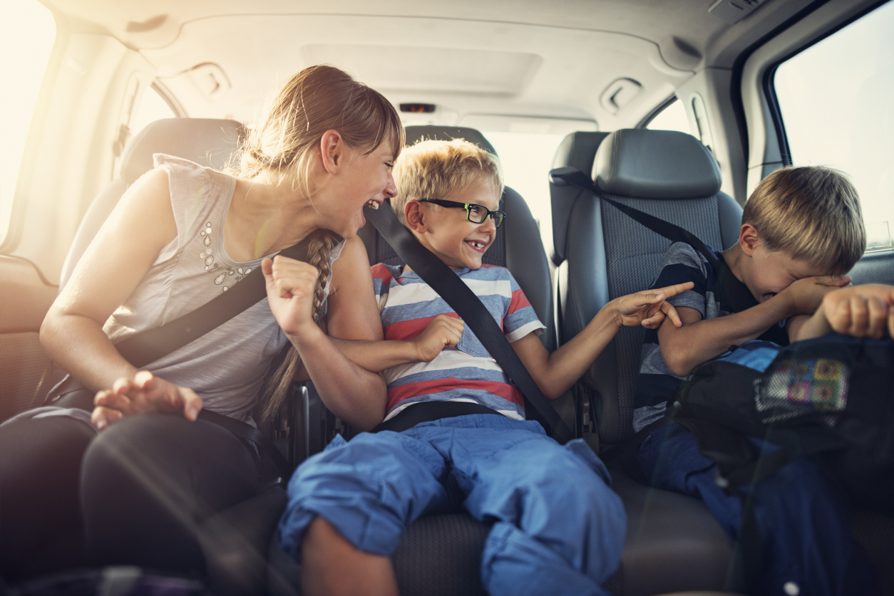 Three kids laughing in car on a road trip.